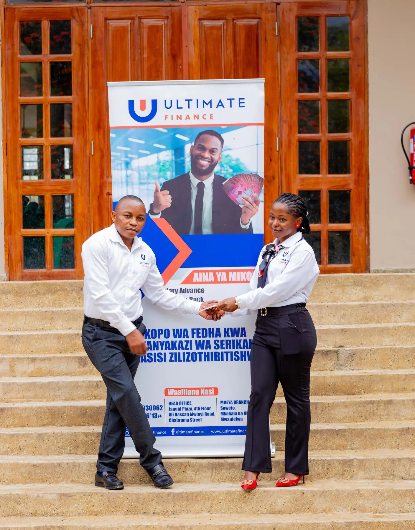 Two members of staff greeting each other beside an Ultimate Finance pull-up banner on office steps