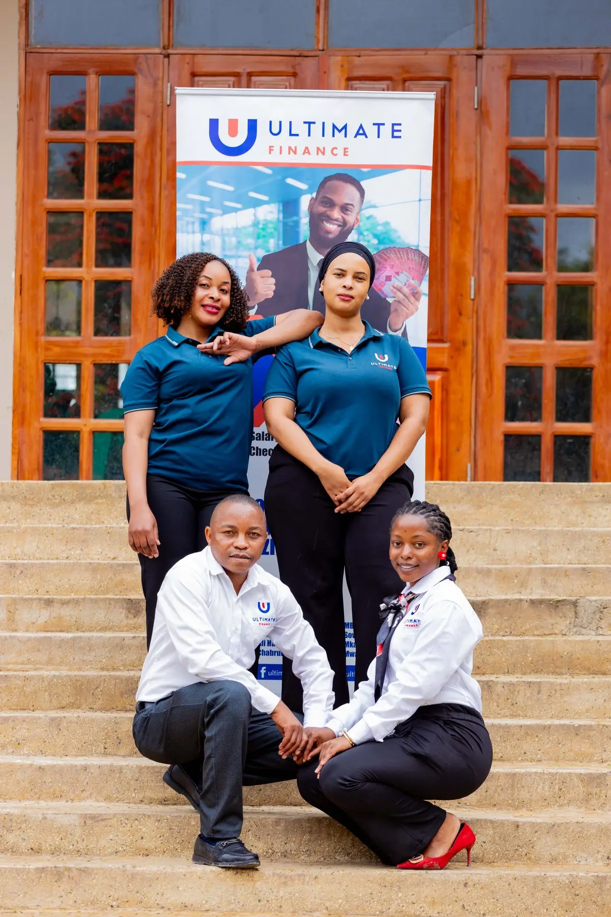 Four members of staff posing beside an Ultimate Finance pull-up banner, two standing in branded polo shirts and two crouching in white shirts