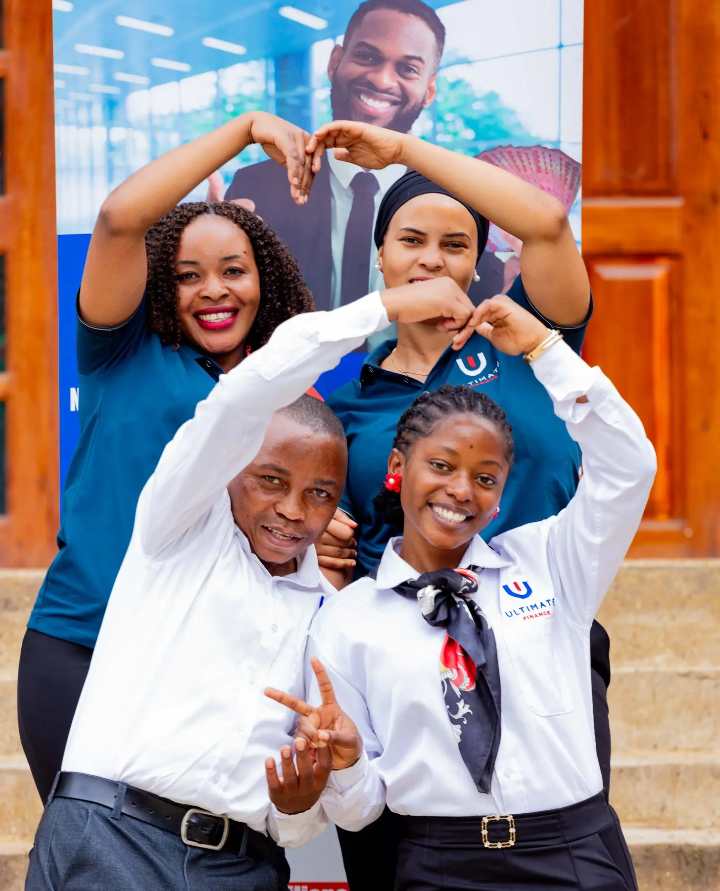 Four members of staff making heart shapes with their hands in front of an Ultimate Finance banner