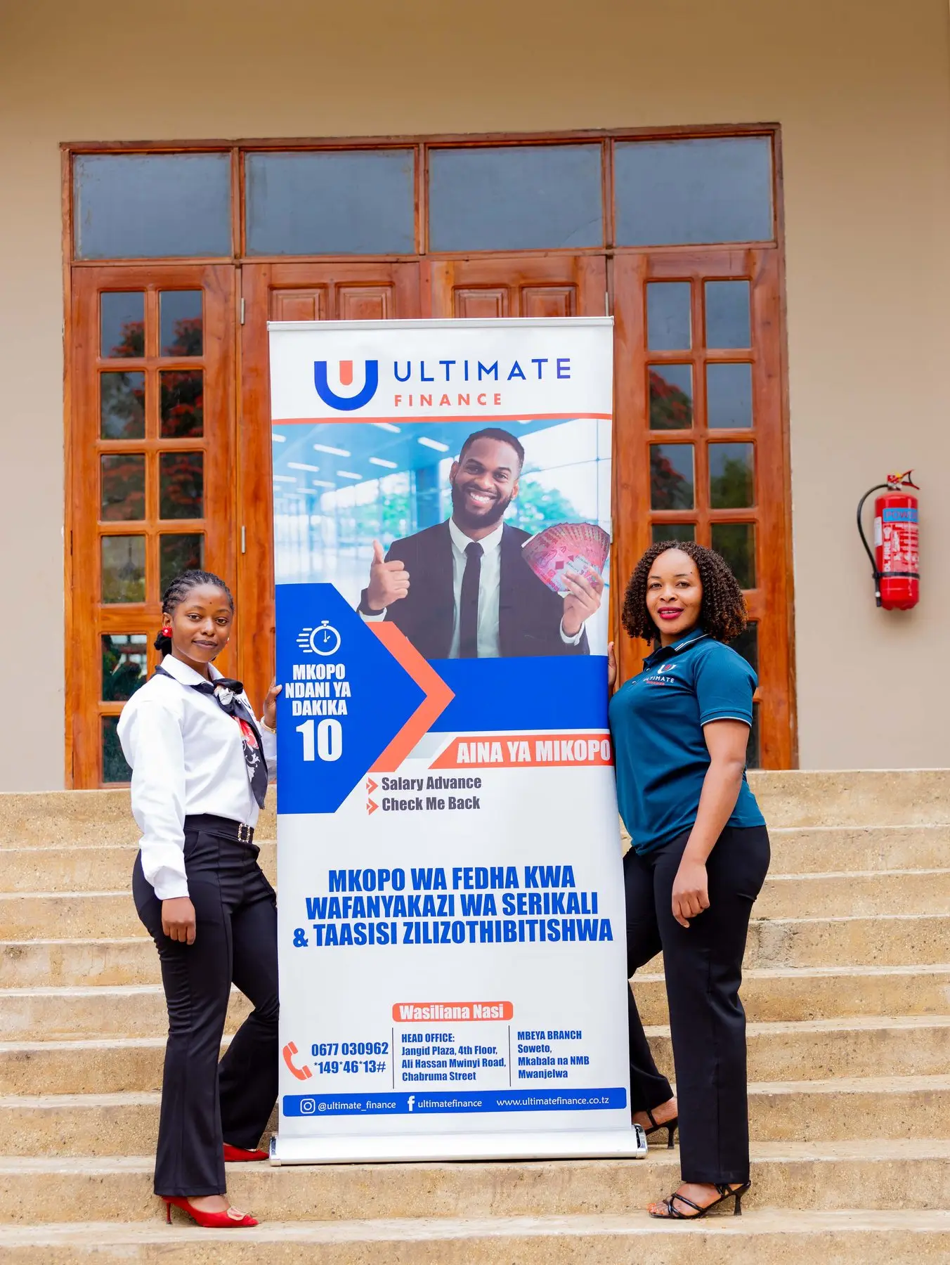 Two members of staff in branded polo shirts standing either side of an Ultimate Finance pull-up banner