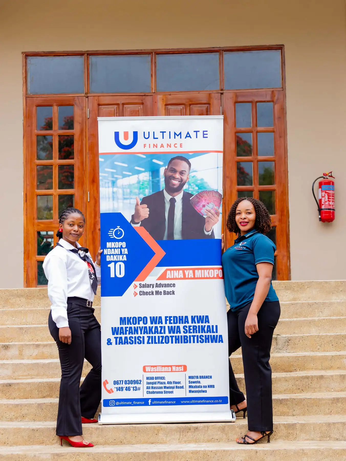 Two members of staff in branded polo shirts standing either side of an Ultimate Finance pull-up banner
