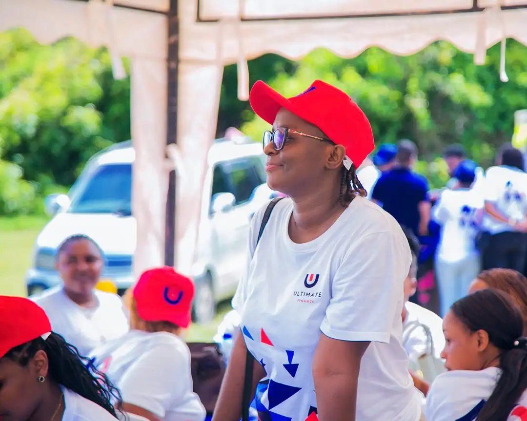 Staff in white branded t-shirts and red caps seated outdoors beneath a canopy