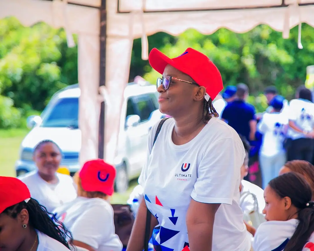 Staff in white branded t-shirts and red caps seated outdoors beneath a canopy