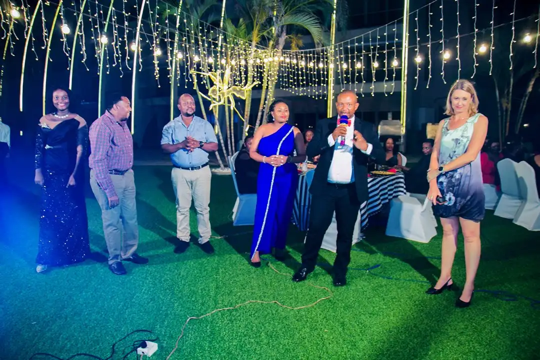 Guests in evening dress standing on a lawn beneath hanging fairy lights at an evening event