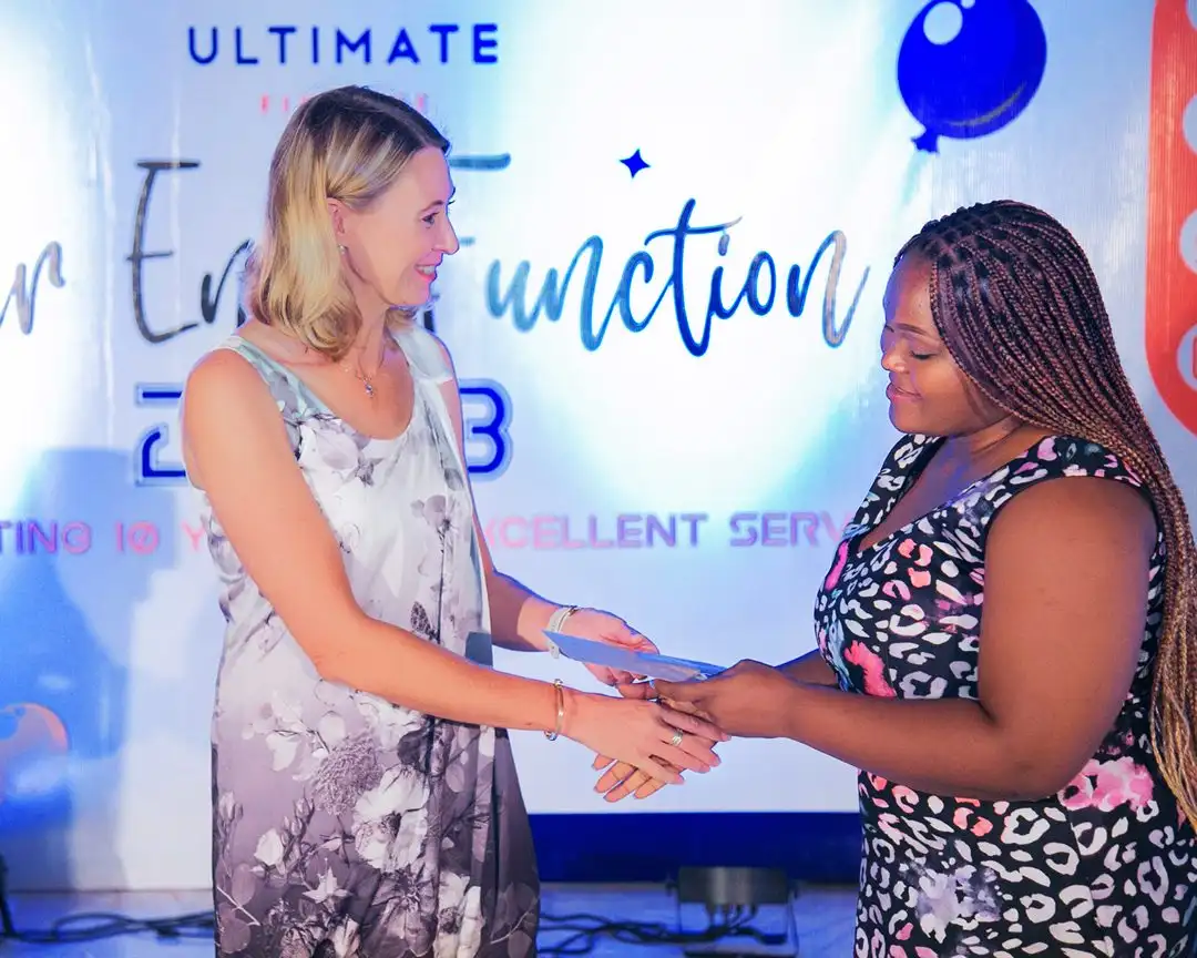 Two colleagues shaking hands as one presents an award, in front of a backdrop reading "Year End Function 2023 – Celebrating 10 Years of Excellent Service"