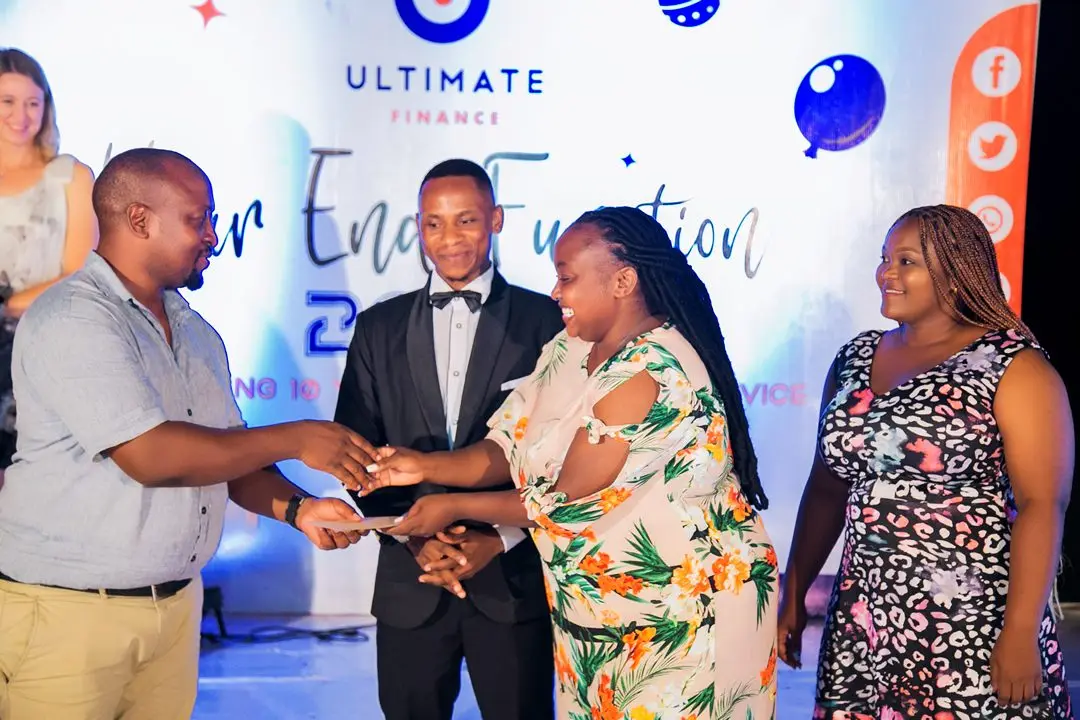Four colleagues on stage as one of them receives an award, in front of the branded backdrop