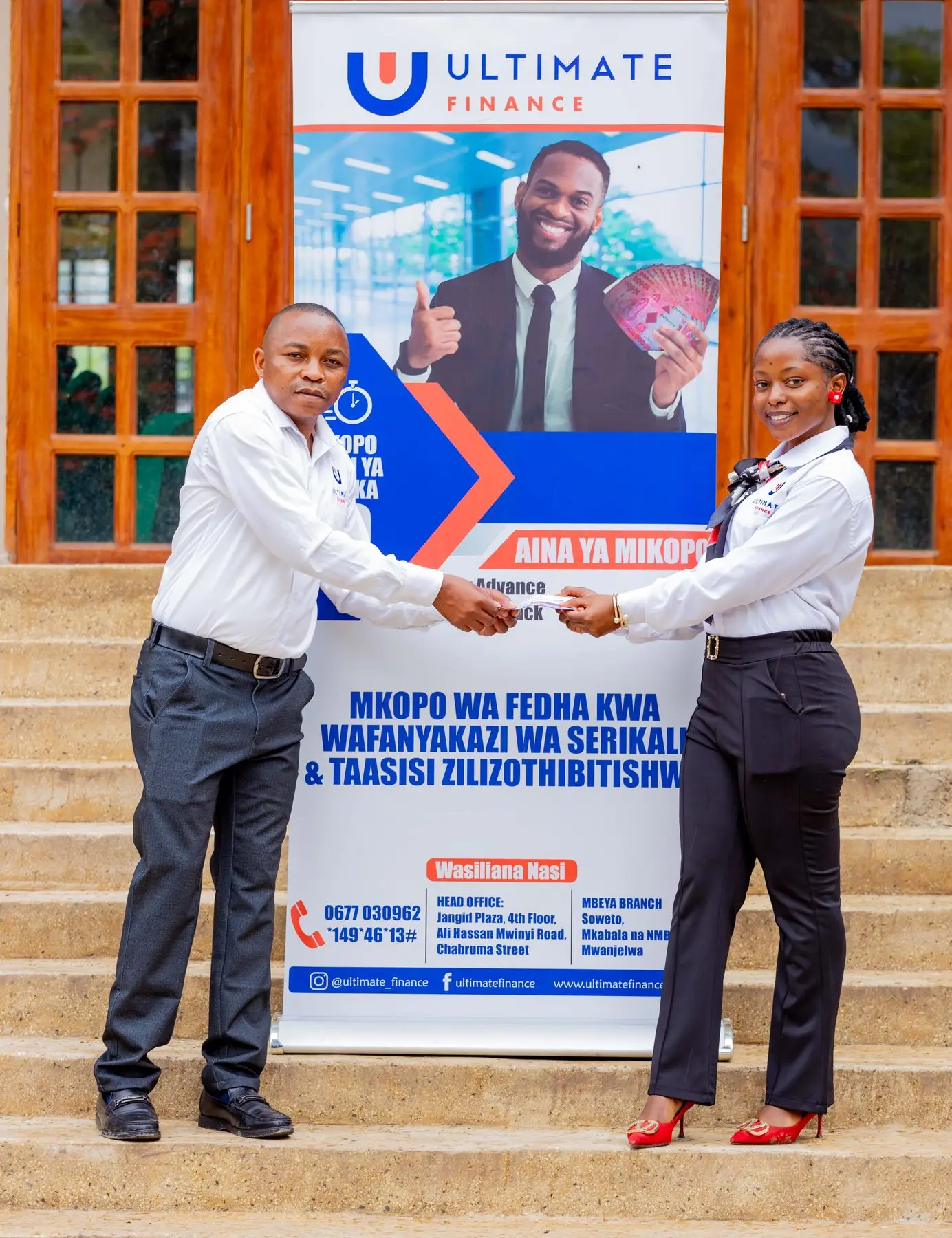 A man and a woman in Ultimate Finance uniform shaking hands in front of an Ultimate Finance pull-up banner on office steps