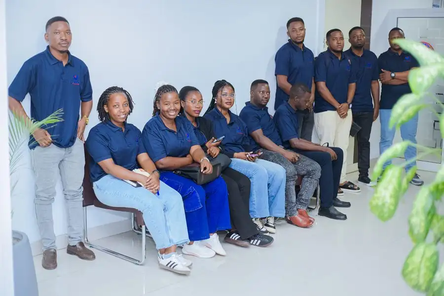 Staff in navy branded polo shirts seated and standing along the wall of a meeting room