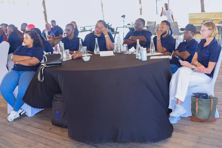 Colleagues seated around a round cloth-covered table beneath a thatched roof at a coastal venue