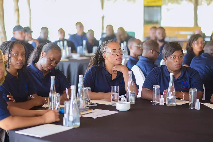 Staff seated along a long conference table taking notes, with water bottles and glasses in front of them