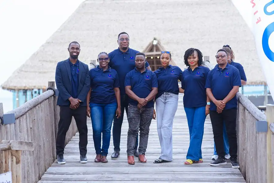 Eight members of staff in navy branded polo shirts standing on a wooden walkway with a thatched roof behind them