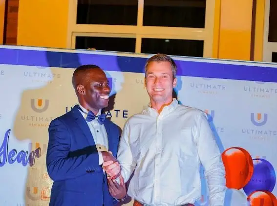 Two men standing in front of an Ultimate Finance branded backdrop at an event