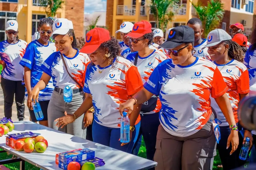 Staff in branded sports jerseys and caps gathered around an outdoor table set with fruit and bottled water at a resort