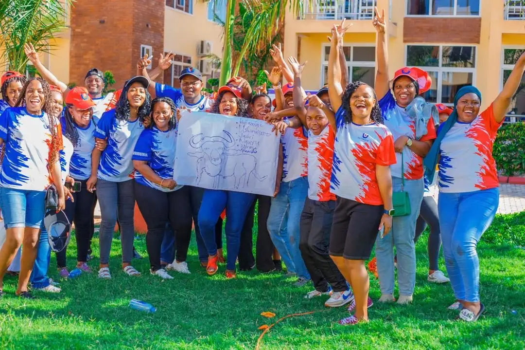 Staff in branded jerseys cheering with their arms raised on a lawn, holding up a placard