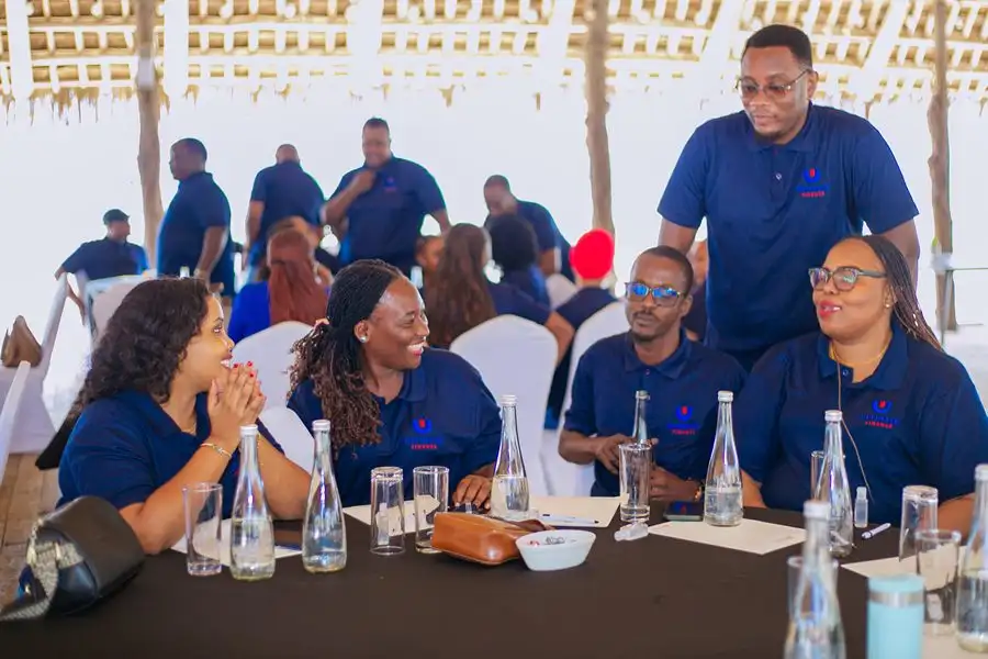 Colleagues around a conference table beneath a thatched roof, one standing behind to talk with those seated