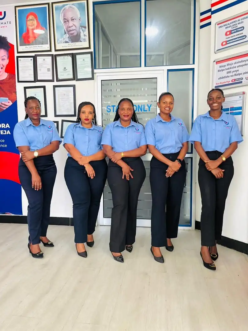 Five members of staff in pale blue branded shirts and black trousers standing together in a branch interior, framed certificates on the wall behind them
