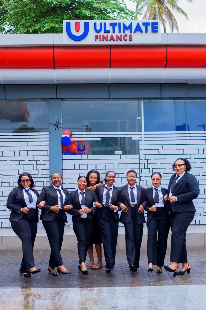 Eight members of staff in dark business suits standing together outside a branch beneath the Ultimate Finance shopfront sign