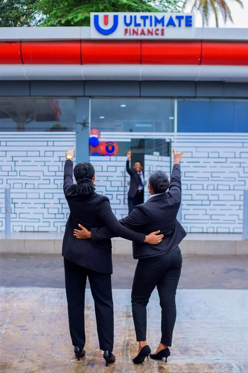 Two members of staff photographed from behind with their arms around one another, looking up at the Ultimate Finance shopfront sign
