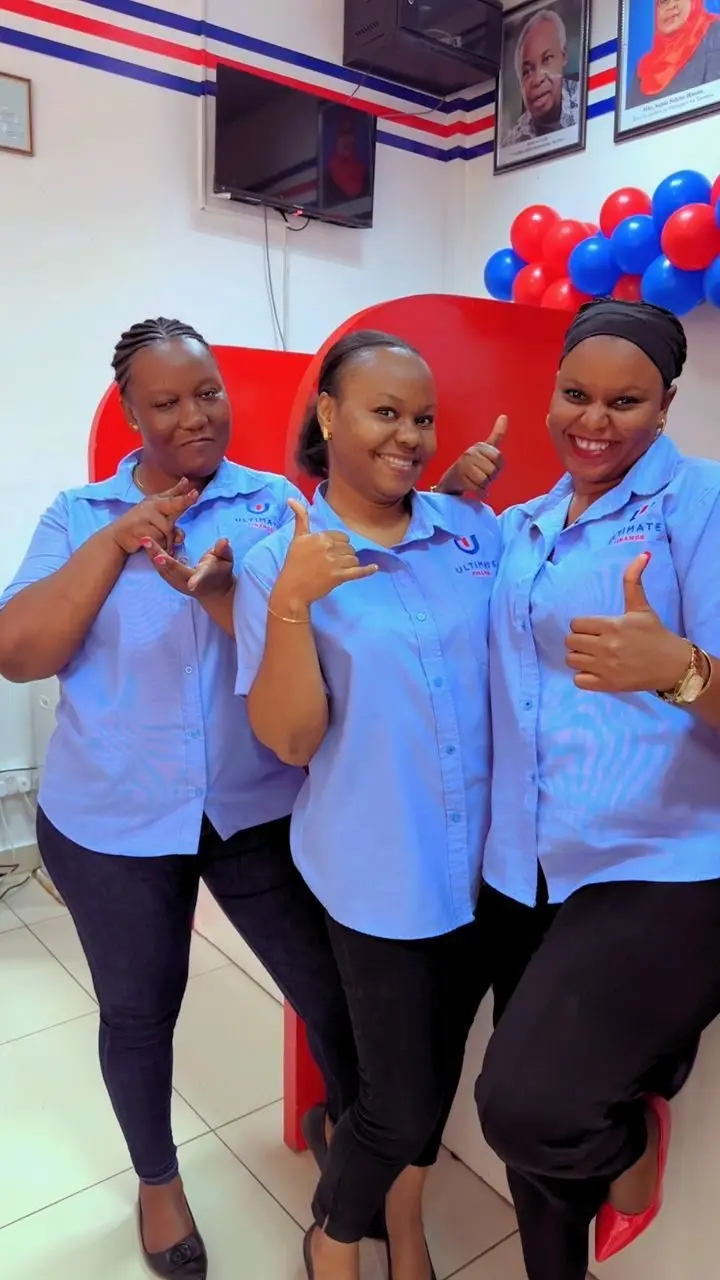 Three members of staff in pale blue branded shirts giving a thumbs-up inside a branch, red and blue balloons behind them