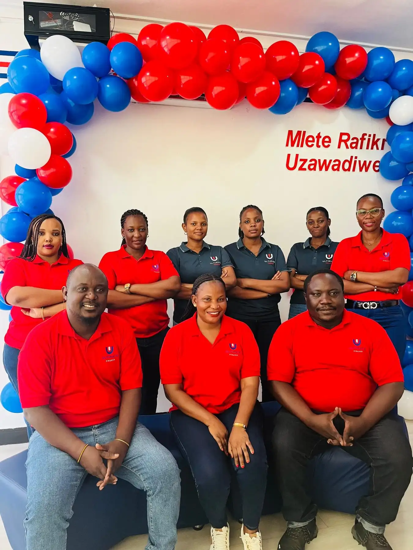 Nine members of staff in red and navy branded shirts posed as a group beneath an arch of red, white and blue balloons
