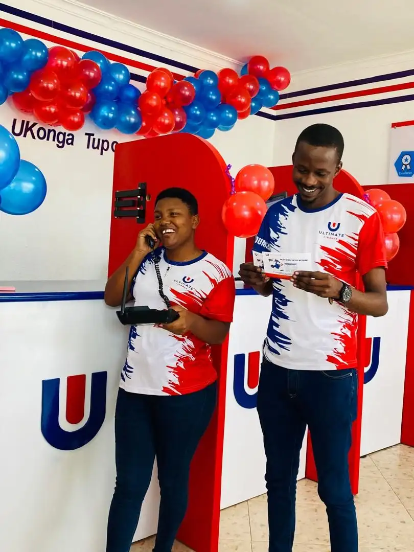 Two members of staff in branded shirts in front of a large painted Ultimate Finance monogram on a branch wall, one of them taking a call