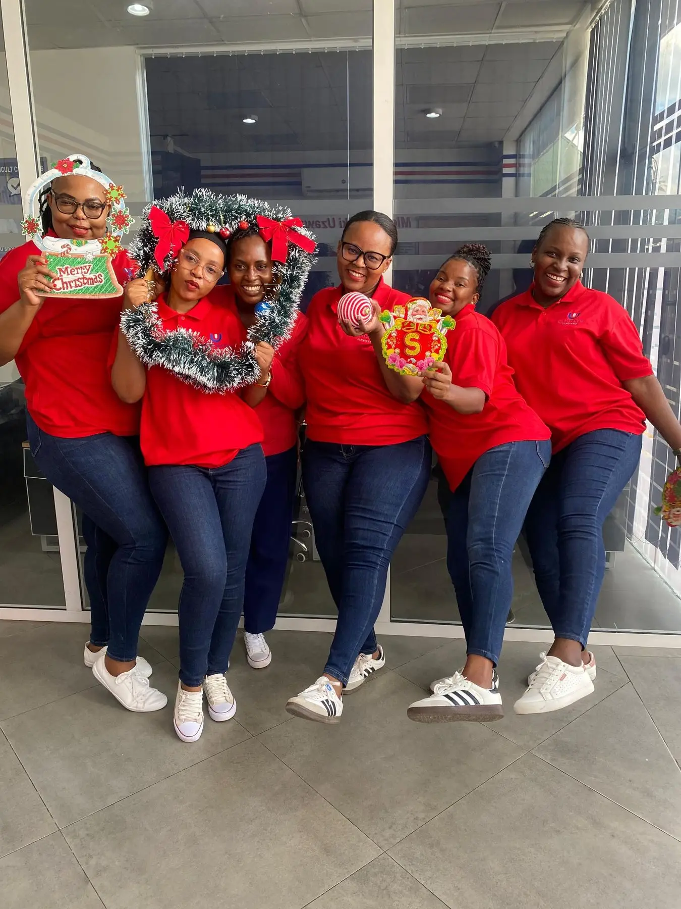 Six members of staff in red shirts and Christmas hats posed together in a branch entrance, holding a tinsel wreath