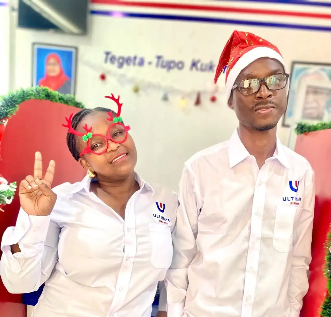 Two members of staff in white branded shirts wearing a Christmas hat and novelty reindeer glasses, in front of a branch wall graphic