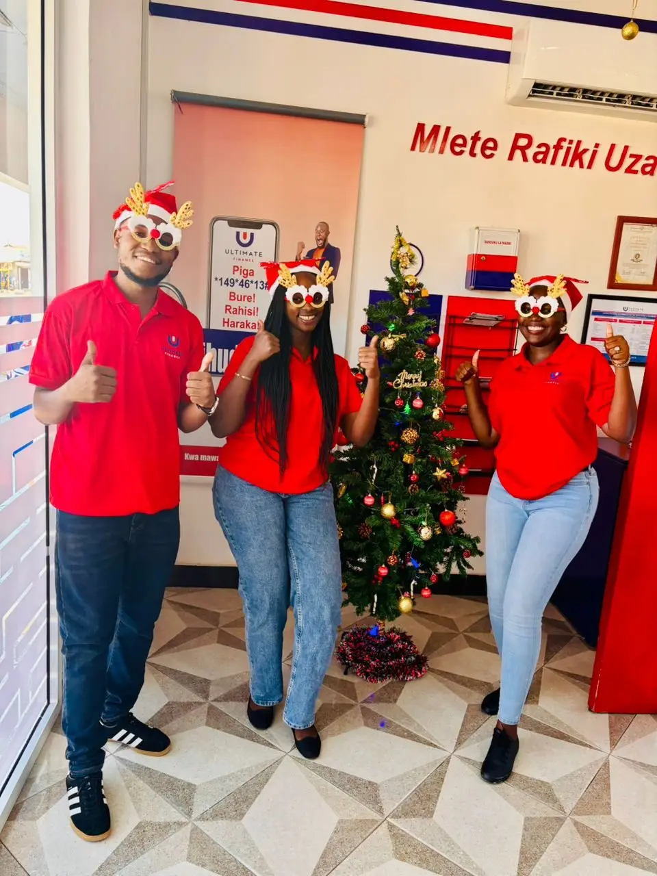 Four members of staff in red shirts and festive novelty glasses beside a decorated Christmas tree in a branch