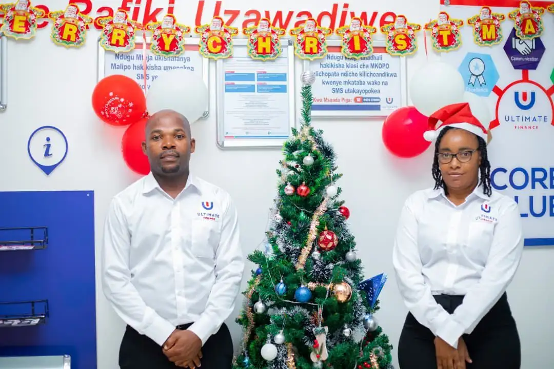 Two members of staff in white branded shirts standing either side of a decorated Christmas tree, beneath Merry Christmas bunting