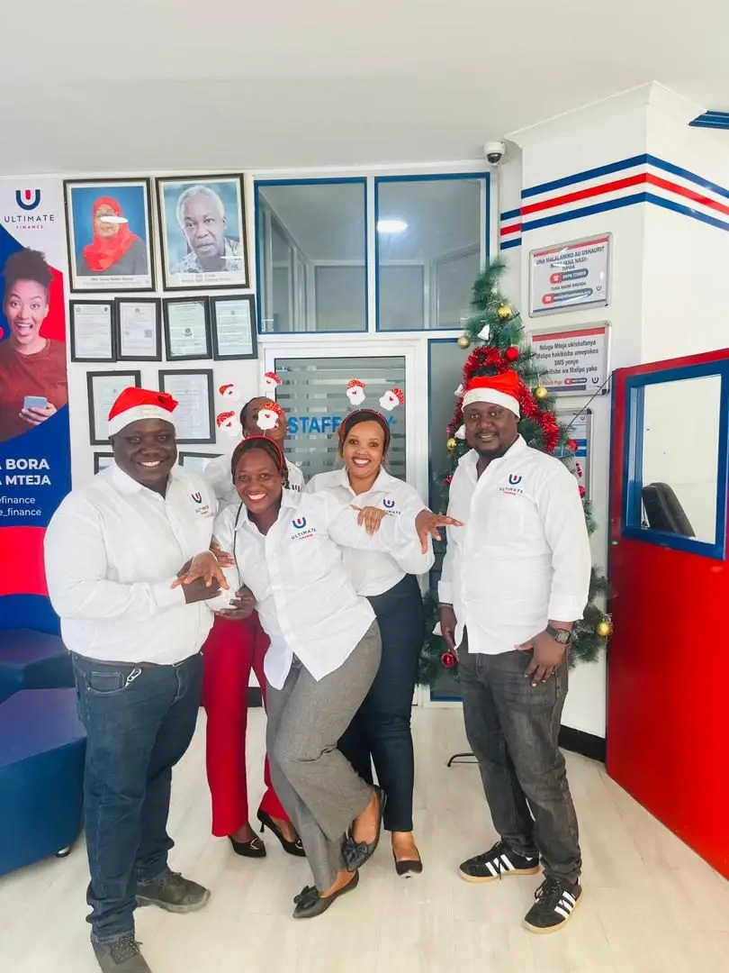 Four members of staff wearing Christmas hats posed together in a branch beside a wall of framed certificates