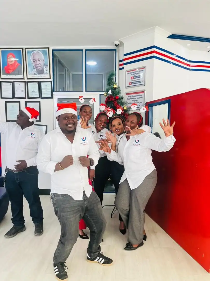 Four members of staff in white branded shirts and Christmas hats posed together in a branch beside a wall of framed certificates