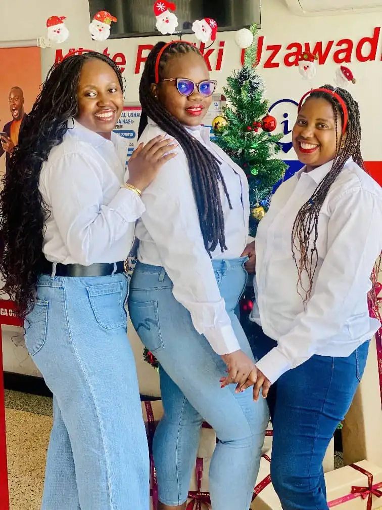 Three members of staff in white shirts and jeans posed beside a Christmas tree, beneath bunting of Father Christmas faces