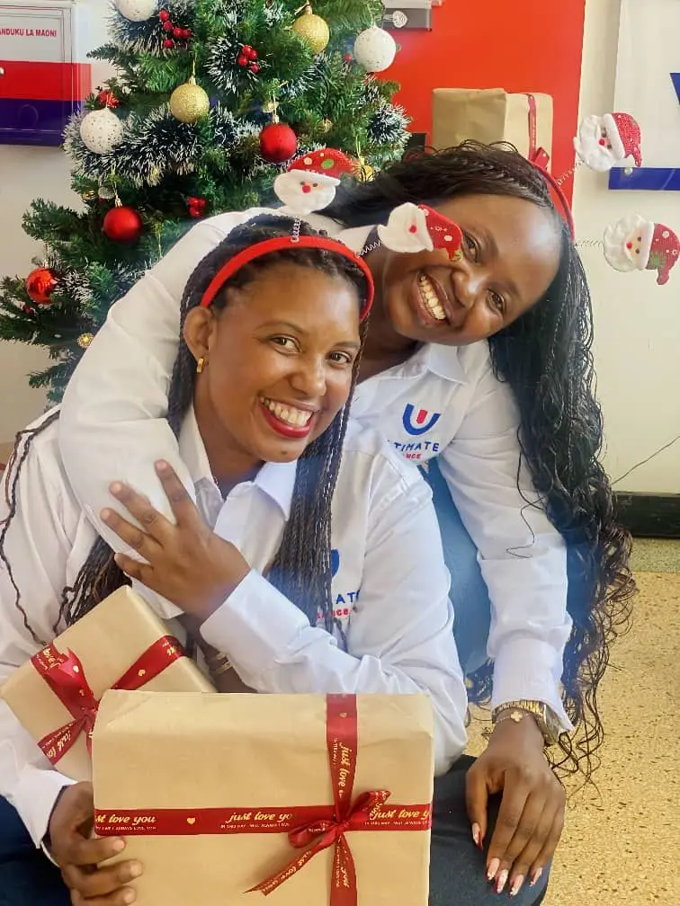 Two members of staff in festive headbands holding a large wrapped gift beside a decorated Christmas tree